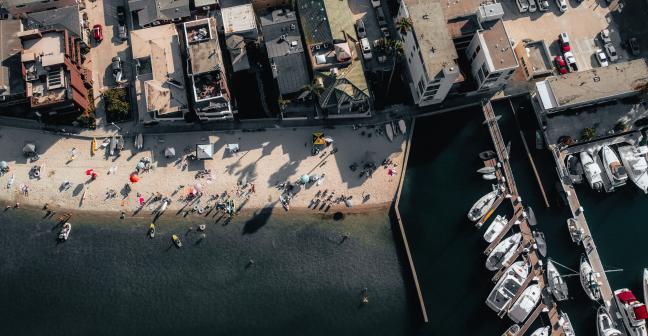 View from above of a beach with people on it, and to the right there are boats along a pier.